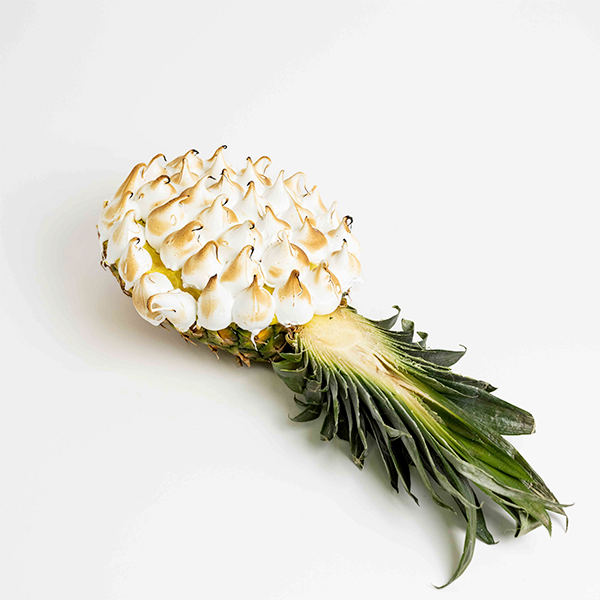 Piña flambeada con merengue dorado elaborada artesanalmente por Formentor, presentada sobre fondo blanco.